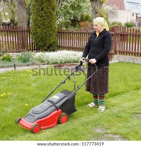 senior woman mowing grass with electric mower in his flower garden