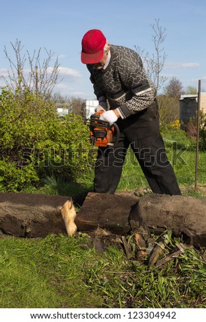an old man in the vegetable garden sawing logs