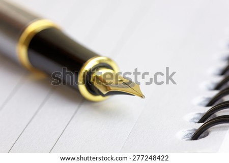 Close up of a gold fountain pen nib on a spiral bound note pad, with shallow d o f