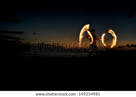 A male fire dancer on a Hawaiian beach spin sticks with fire to create circles of flames.