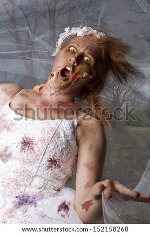A grotesque and bloody female zombie dressed in a wedding dress and veil runs through the woods