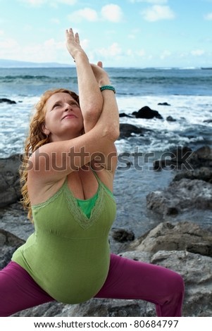 Pregnant woman in a eagle pose as she performs yoga on a beach in Maui, Hawaii.