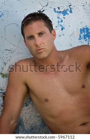 Shirtless man looking into camera, blue wall in the background