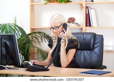 portrait of smiling young woman working on the computer while talking on the phone