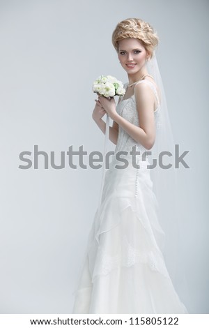 picture of happy young woman in bridal gown with flowers posing over gray background