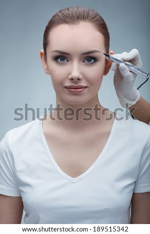 closeup portrait of lovely young woman getting permanent makeup on her eyebrows