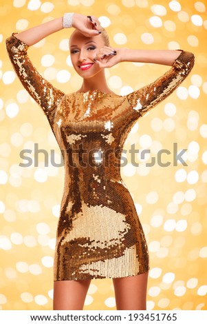 picture of happy beautiful young woman wearing gold dress posing against gold background