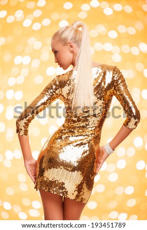 picture of beautiful young woman wearing gold dress posing against gold background