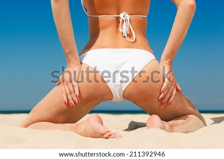 back view of female buttock in white bikini kneeling on the sand against sea