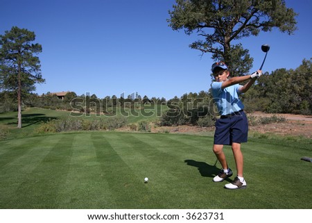 Young male golfer about to hit a ball on a beautiful golf course with blue sky