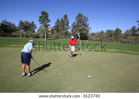 Father and son golfing where son is putting and father is holding the flag