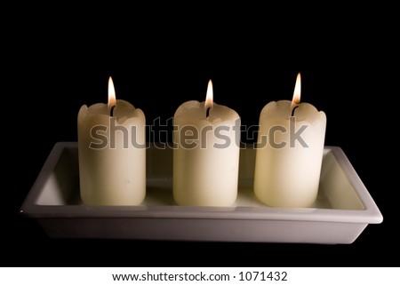 Three white candles lined up in a white saucer isolated on black