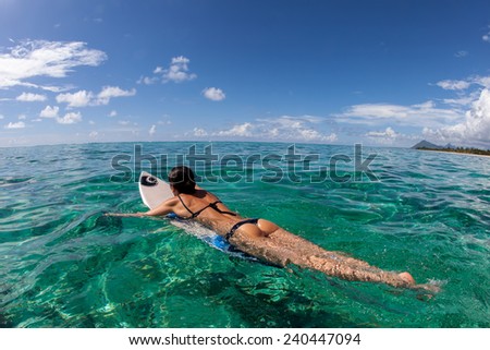 beautiful young girl surfer swims in the clear waves. She rides in the Indian Ocean island of Mauritius