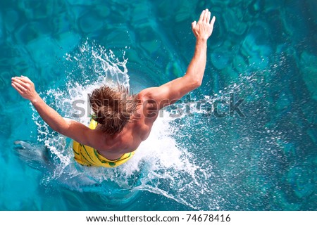 a young man jumps into the turquoise water of the Red Sea