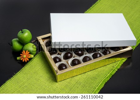 Golden box of chocolate with green apples / Box of chocolates open / Opened box with chocolate balls on green raw textile