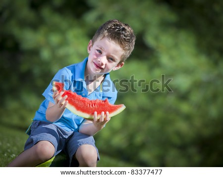 Happy boy sitting outside eating a water melon slice