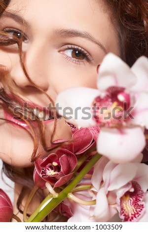 The beautiful girl with curly dark hair. In hair of an orchid