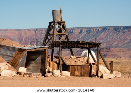 A wester scene with a mine shaft and water tower in the desert.