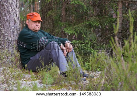Old man resting in a forest near a tree