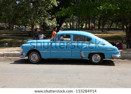 MORON, CUBA - FEBRUARY 19: People walk past old car on February 19, 2011 in Moron, Cuba. Recent change in law allows Cubans to trade cars again. Most cars in Cuba are very old because of the old law.
