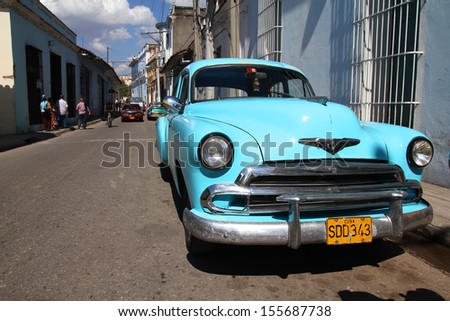 SANCTI SPIRITUS, CUBA - FEBRUARY 6: People walk past old car on February 6, 2011 in Sancti Spiritus.  Recent change in law allows the Cubans to trade cars after it was forbidden for many years.