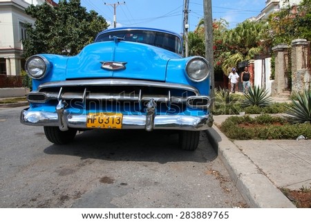 HAVANA, CUBA - FEBRUARY 24, 2011: People walk by oldtimer car parked in the street of Havana, Cuba. Cuba has one of the lowest car-per-capita rates (38 per 1000 people in 2008).