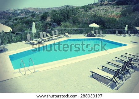 Generic vacation resort in Crete island in Greece. Swimming pool sun tanning chairs. Vintage style - filtered colors.