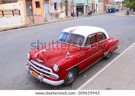 CAMAGUEY, CUBA - FEBRUARY 17, 2011: People walk past old car parked in the street in Camaguey, Cuba. Cuba has one of the lowest car-per-capita rates (38 per 1000 people in 2008).