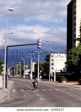 Lonely man on a bicycle, rows of lamp posts and an empty road in the French city of Grenoble