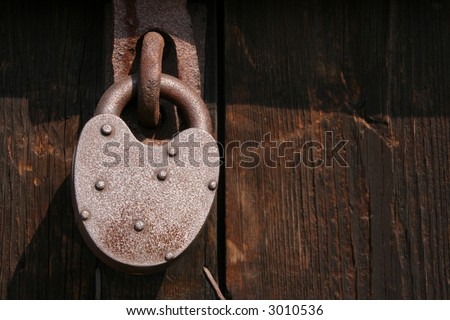 Old rusty pad lock on wooden door.