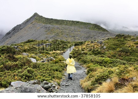 Lonely tourist in yellow plastic raincoat. Rainy weather on a Hooker Valley trail near Mt. Cook, New Zealand.
