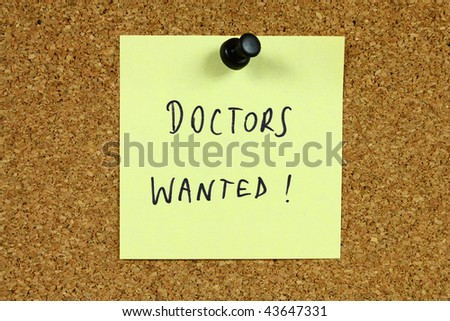 Yellow sticky note pinned to an office notice board. Doctors wanted - employment and medical career recruitment message.
