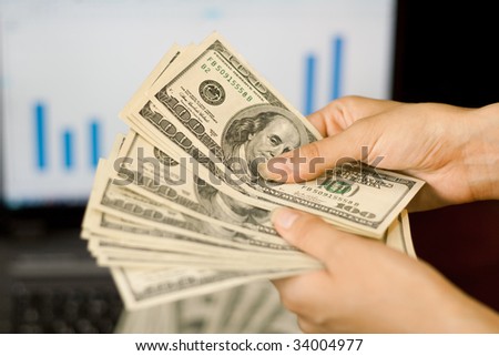 person counts money in hands near the laptop