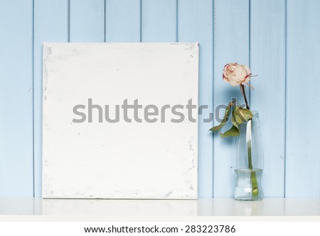A blank shabby canvas and white rose in the bottle on blue wooden background