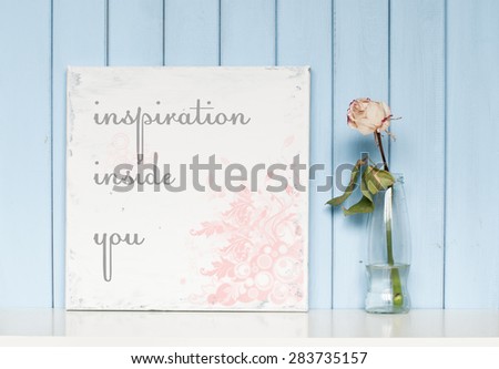 shabby vintage poster with quote Inspiration inside you and white rose in the bottle on blue wooden background