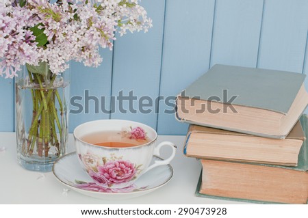 Gentle bunch of lilac, vintage books and china teacup on the table on blue wooden background
