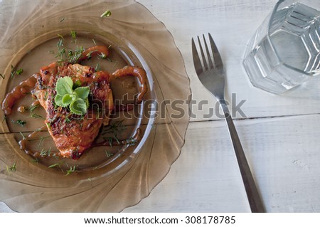 Chicken with crispy golden crust cooked in oven and served with greens and sauce, glass of water, fork and