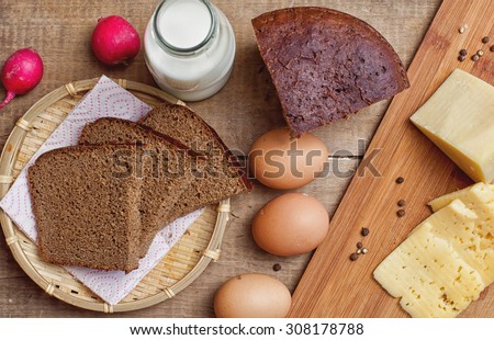 Red radish, bottle of milk, rye bread, cheese, hen eggs on wooden table