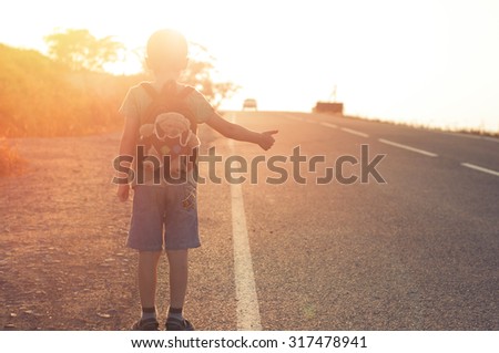 Little child hitchhiking alone summer sunset background