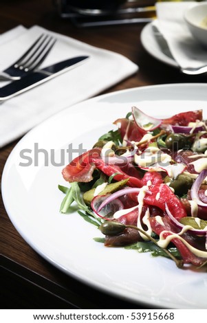 Fresh salad with prosciutto,various vegetables and  tartar sauce  in restaurant setting with white wine