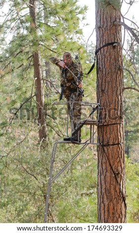 Bow hunter in a ladder style tree stand with bow at full draw, demonstrating good safety by using a safety harness