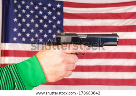 close-up of a man\'s hand holding a semi-automatic pistol in front of an American flag