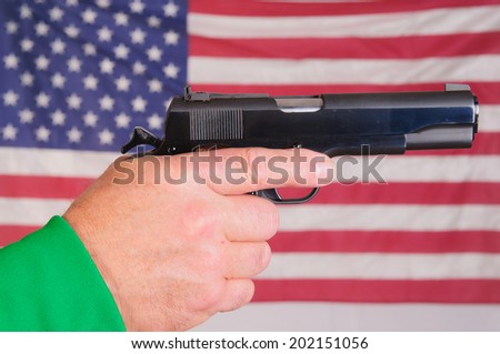 Close-up of a man\'s hand holding a cocked .45 ACP semi-automatic handgun infront of an American flag