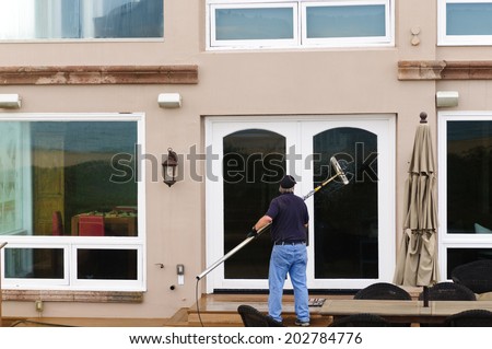 Professional window washer cleaning house windows with de-ionized water using an extension pole