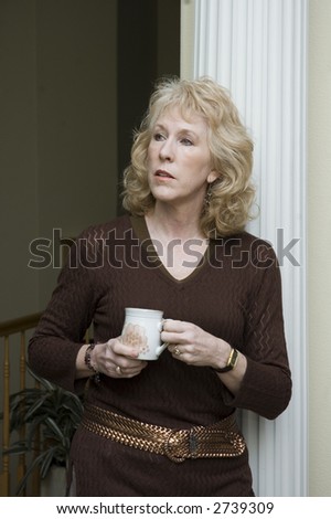 Older blond woman leaning against a column enjoying a cup of coffee