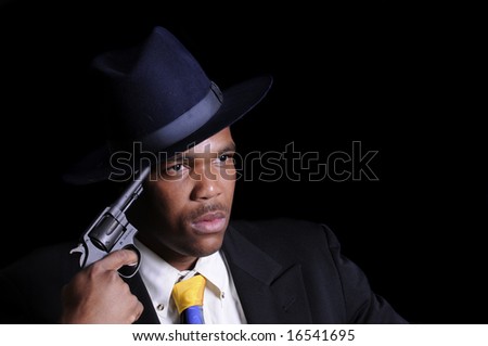 young African American man in a hat and suit with gun to his head isolated on black