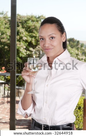 Beautiful African-American woman holding a glass of white wine while standing at a window