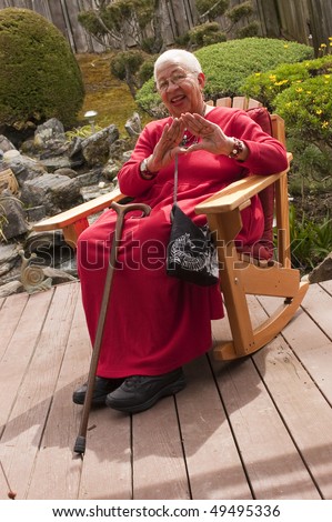 an elderly smiling african american woman, a member of Delta theta  sitting in a rocking chair in her garden making a Delta sign with her hands