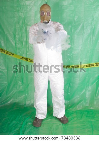 Man in Hazmat clothing in temporary green plastic decontamination chamber wearing a gas mask and carrying toxic chemical that is exuding gaseous vapor