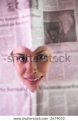 happy woman outdoor looking through a newspaper cut out in shape of heart